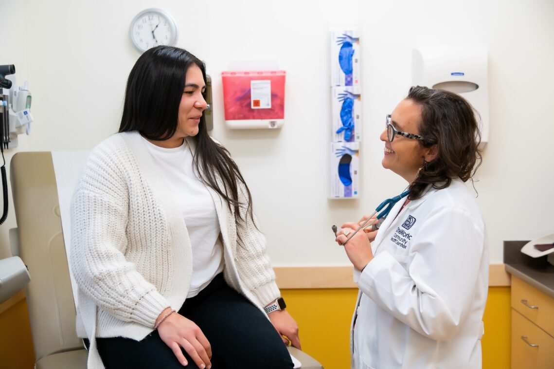 A patient sits on the exam table while speaking with a provider.