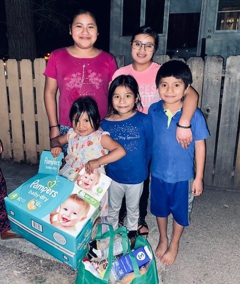 A group of children posing for a photo holding a box of diapers and baby supplies.