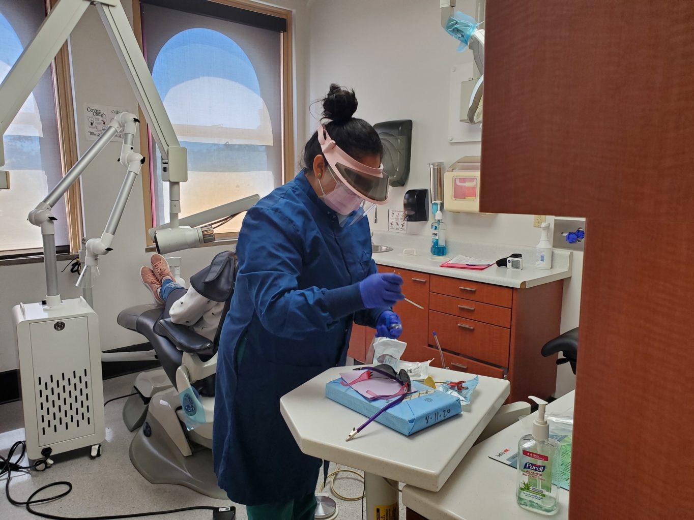 A dental hygienist in a blue coat and mask working on a dental treatment
