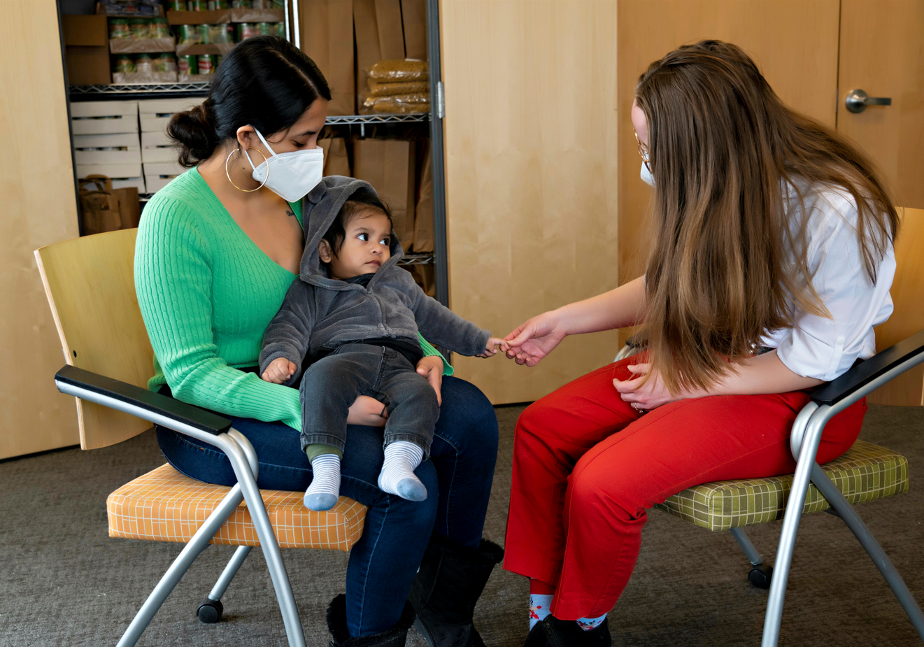 Wesley speaks with Thiago and his mother at the OneWorld dry food pantry. They are sitting down and wearing masks.