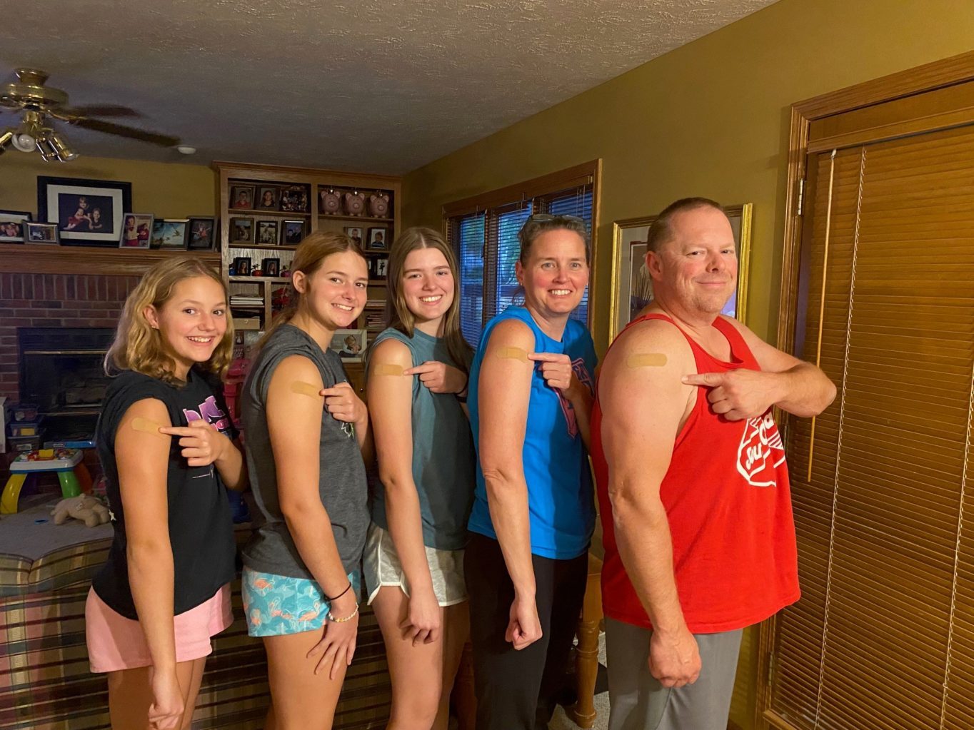 A group of people pointing at their bandaids on their forearm from a vaccination