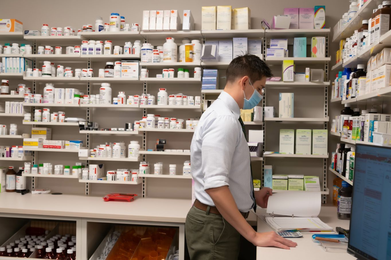A person wearing a mask standing in front of a shelf with medicine