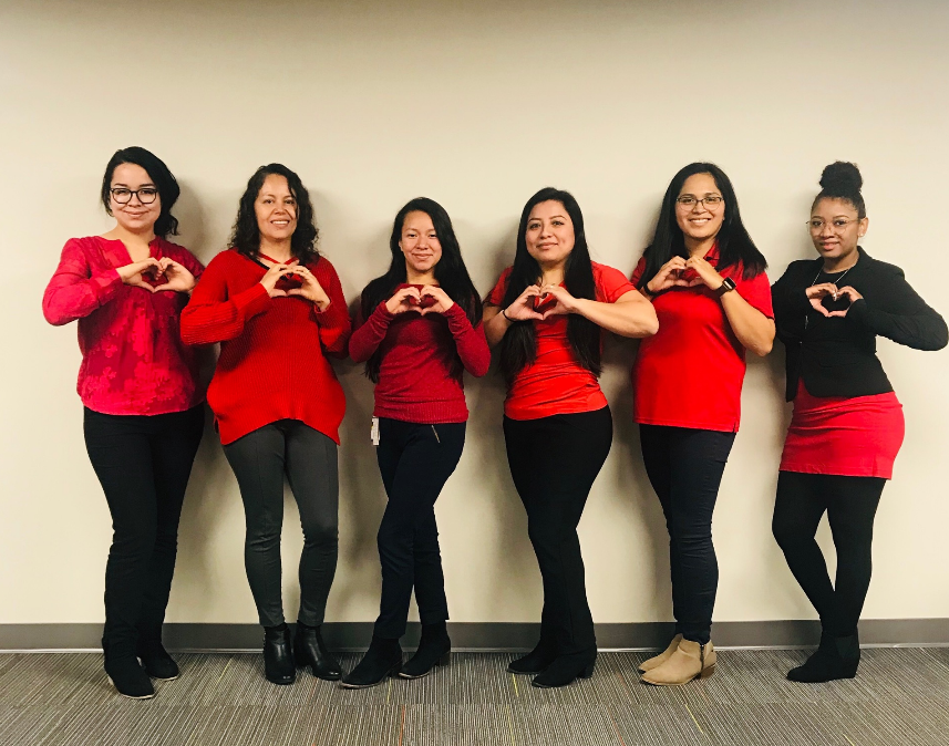 A group of women in red shirts making a heart with their hands