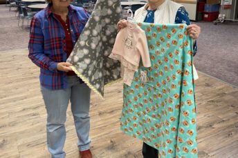 Two older ladies smiling and holding baby blankets.