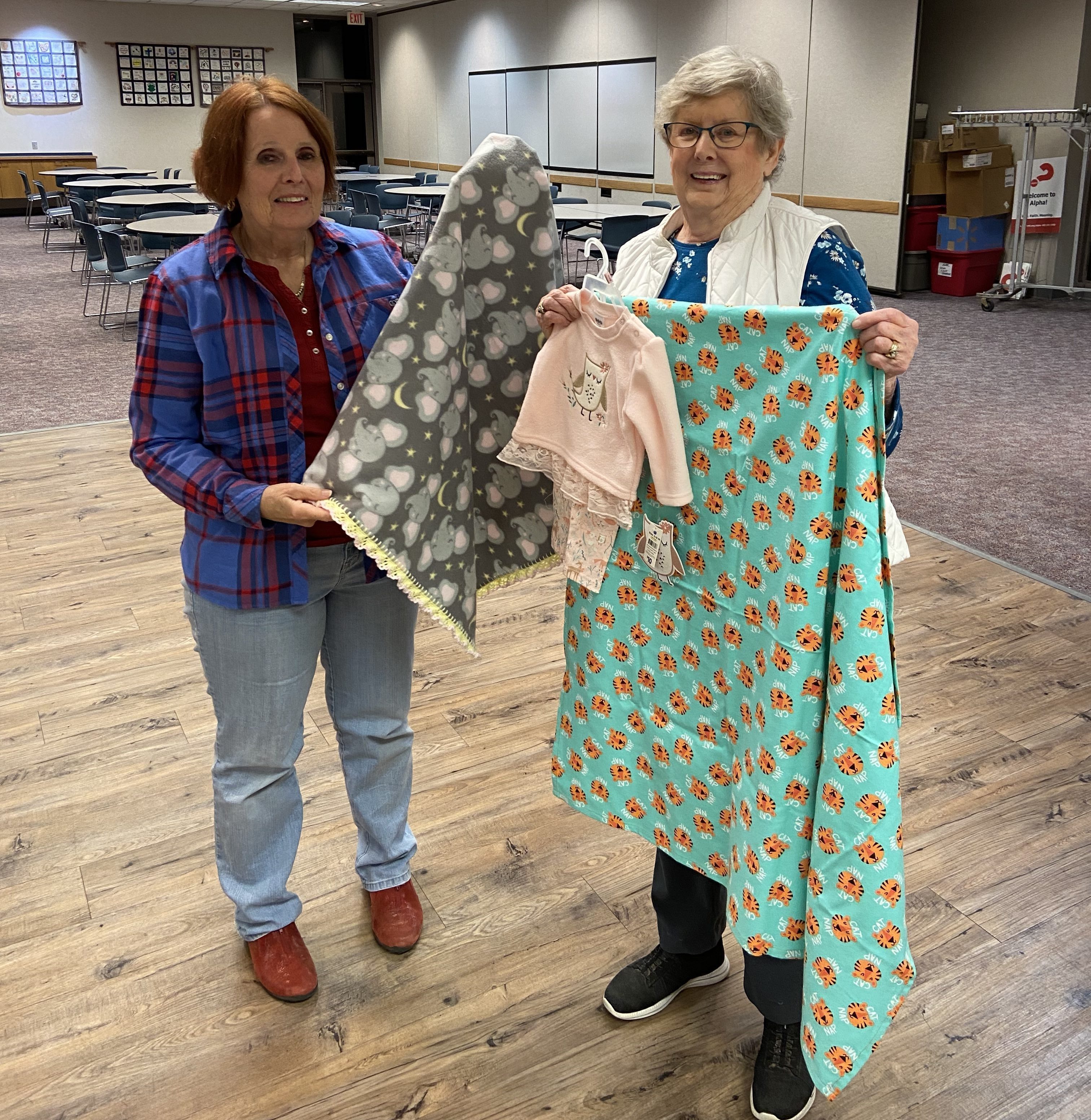 Two older ladies smiling and holding baby blankets.