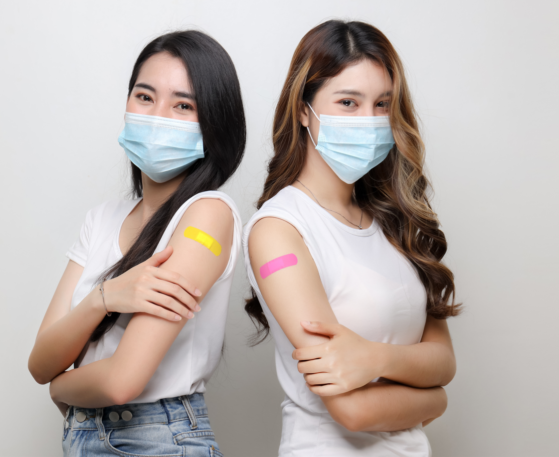 Twoyoung women wearing face masks with bandaids on their upper arm