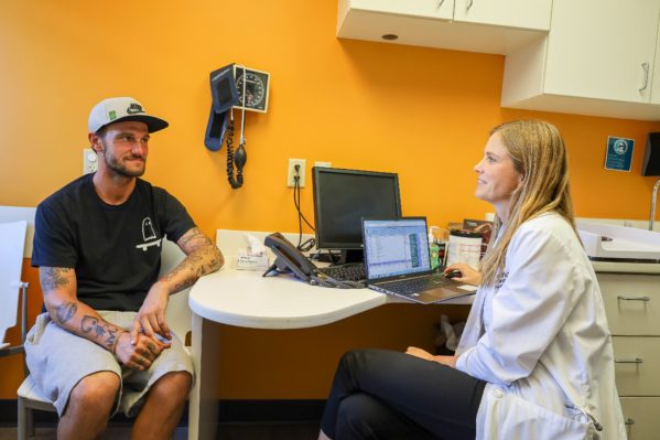 A female provider sitting down at her desk and facing a male patient sitting across her.