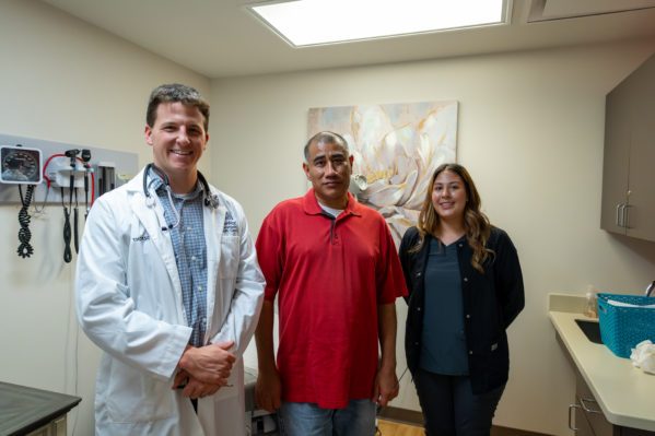 Clinician and Health Assistant stand with patient in exam room. 