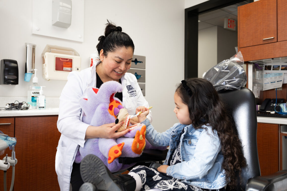 Dental Hygienist Mayra Perez helps a young patient practice brushing, using a stuffed animal.