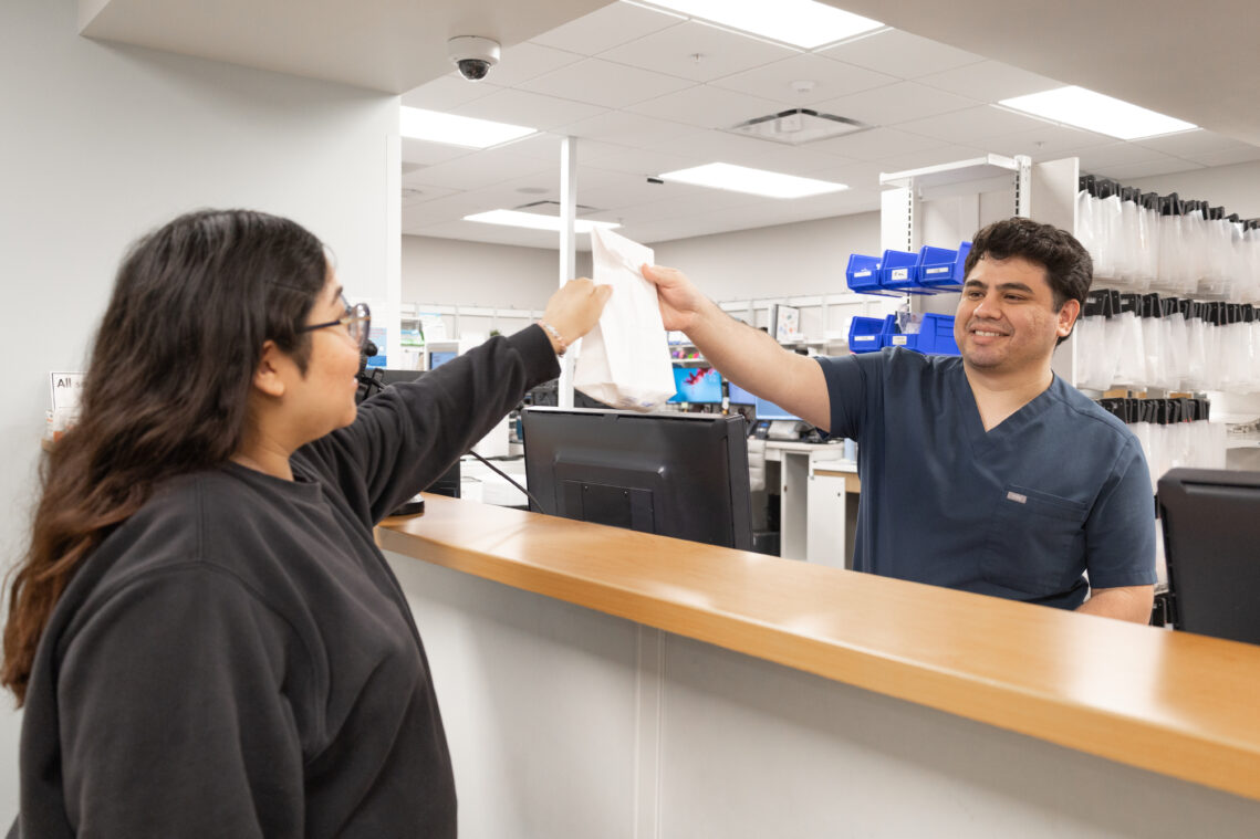 Pharmacy Technician Enrique Marquez hands prescription medications to a patient.
