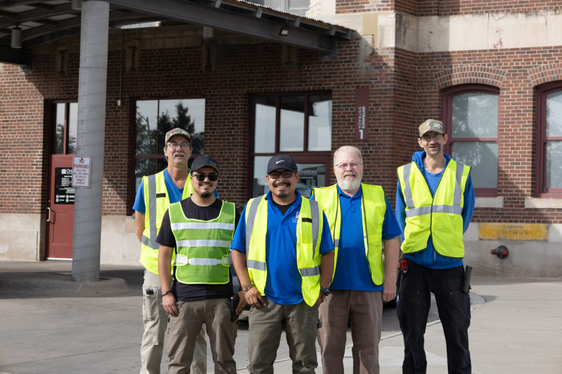 Facilities personnel from OneWorld and the building management company gather in front of the main Livestock Exchange Campus building.