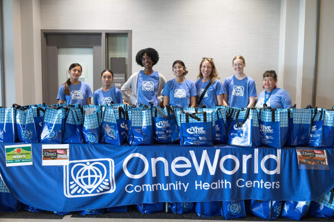 A group of volunteers holds tote bags, and a OneWorld banner stretches in front of them.